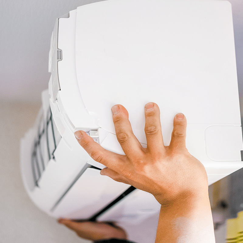 Mains d'une personne soulevant le couvercle d'un climatiseur mural blanc, en cours d'installation ou de maintenance.