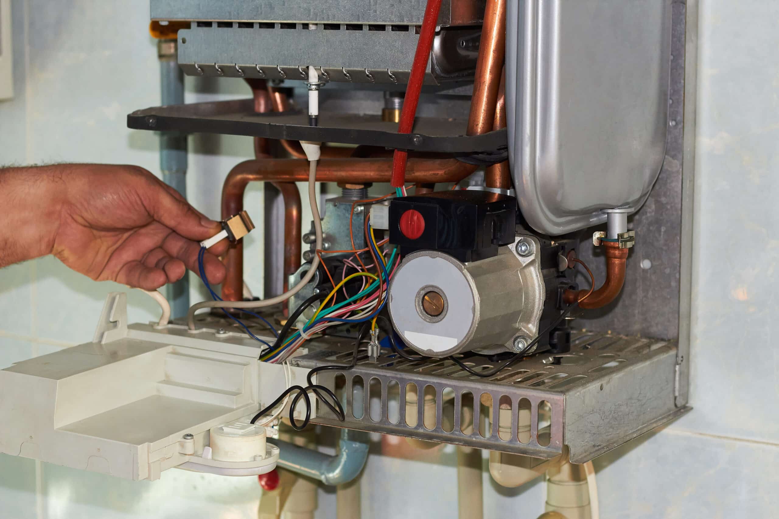 Technicien réparant une chaudière à gaz murale, avec ses composants internes exposés: tuyaux cuivre, câbles et moteur.